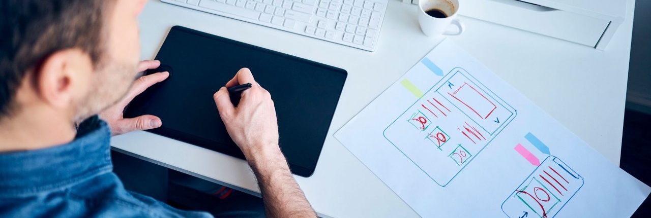 Male web designer working on a website's responsive design using computer and hand-drawn drafts