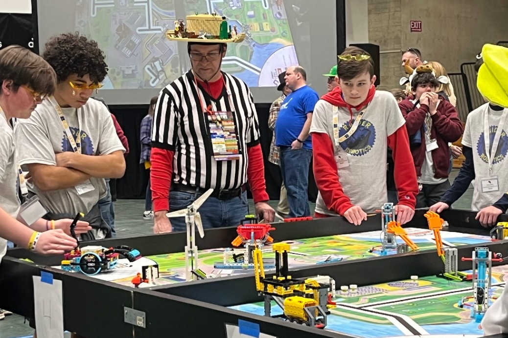 Middle school Robotics teams compete in the Robot Games while a referee stands by