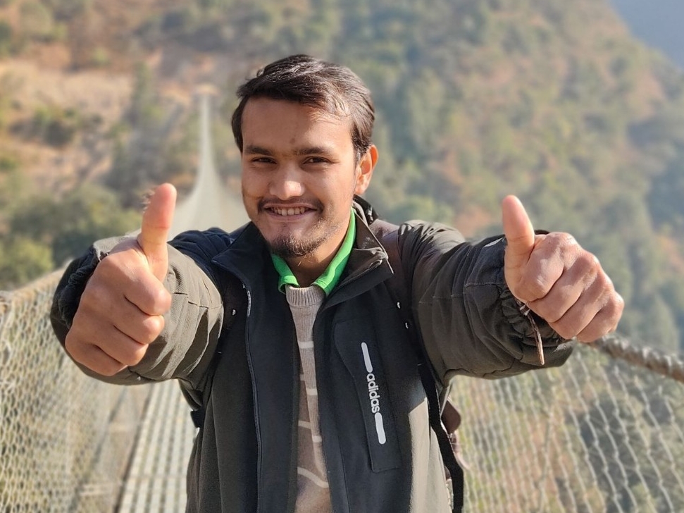 Bikash Acharya giving two thumbs up for the camera outside on a bridge.