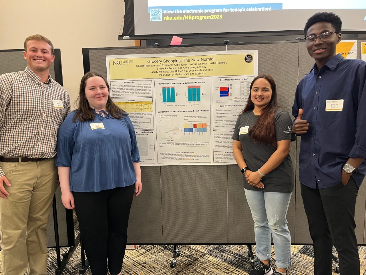 Four NKU students smiling in front of a poster presentation of their research