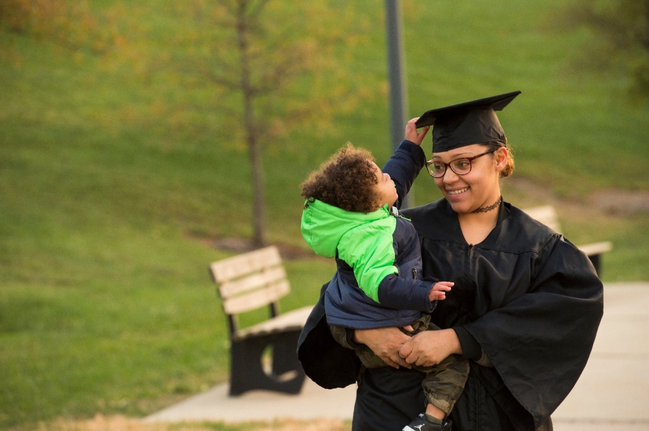 Student parent holding child while in graduation regalia